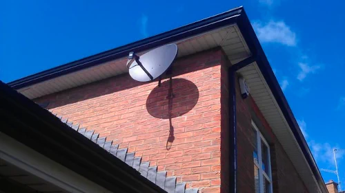 Antena satelitarna z konwerteram na 4 kable zamontowana na ceglanej elewacji budynku z błękitnym niebem w tle