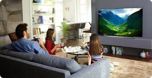 Trzy osoby w pokoju oglądające telewizję na dużym telewizorze