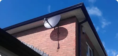 Satelitarna antena cyfrowa zainstalowana na ścianie z cegły niedaleko dachu