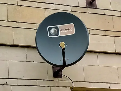 Satelitarna antena Polsat Box Szara antena satelitarna z logo Cyfrowy Polsat przymocowana za pomocą stalowego uchwytu w ciemnym kolorze do ceglanej ściany